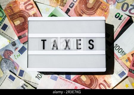 Tableau lumineux avec mot TAXS en lettres noires autour des billets en euros. Paiement d'impôt et présentation de déclarations. Argent, affaires, finances, Banque D'Images