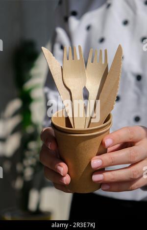 Les femmes tiennent des fourchettes en bois et des gobelets en papier avec des assiettes. Vaisselle jetable écologique. Utilisé dans la restauration rapide, les restaurants, Banque D'Images