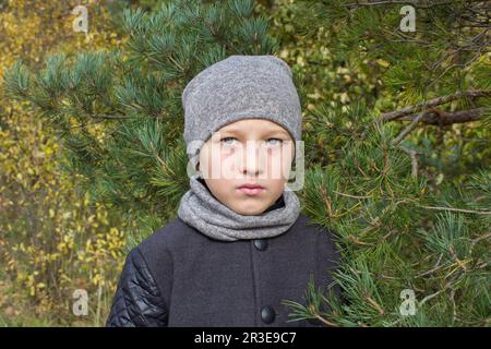 Entre les pins, le garçon est à la mode dans un manteau Banque D'Images