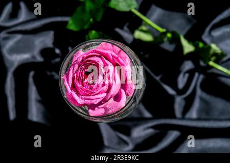 Verre à vin rempli d'une table de pétalson à fleurs roses avec tissu en soie noire. Une vie moderne et minimale. Concept de vacances Valentines Banque D'Images