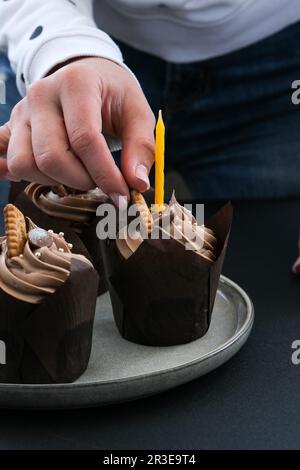 Les mains des femmes font de délicieux petits gâteaux au chocolat avec de la crème sur fond sombre. Trois muffins au chocolat. Gâteau d'anniversaire préparation Banque D'Images