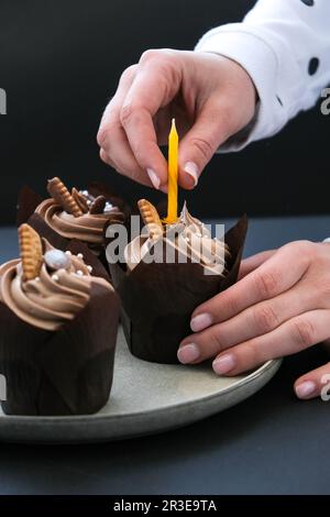 Les mains des femmes font de délicieux petits gâteaux au chocolat avec de la crème sur fond sombre. Trois muffins au chocolat. Gâteau d'anniversaire préparation Banque D'Images