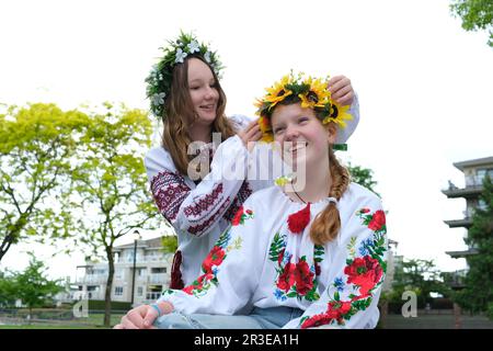 Deux belles filles ukrainiennes tissage couronnes chemises brodées verdure nature s'asseoir près de la maison divertissement ukrainien à des parties reste communication chanter des chansons rites nationaux rire sourire parler Banque D'Images