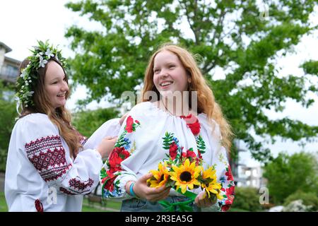 Deux belles filles ukrainiennes tissage couronnes chemises brodées verdure nature s'asseoir près de la maison divertissement ukrainien à des parties reste communication chanter des chansons rites nationaux rire sourire parler Banque D'Images