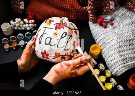 BRICOLAGE. Faites-le vous-même. Une femme peint des décorations d'action de grâce sur la citrouille d'orange pour Halloween. Récolte d'automne. Banque D'Images