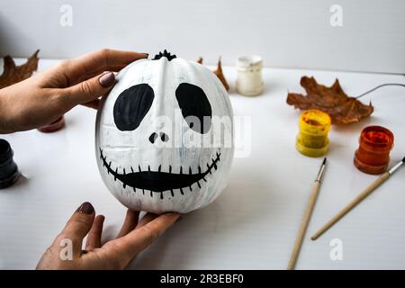 Une femme peint le visage sur la citrouille d'orange pour Halloween. Feuilles d'automne. Bricolage pour enfants. Faites-le vous-même. Banque D'Images