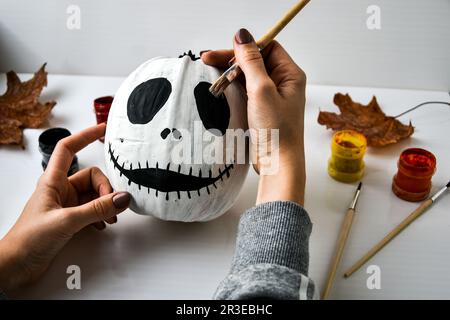 Une femme peint le visage sur la citrouille d'orange pour Halloween. Feuilles d'automne. Bricolage pour enfants. Faites-le vous-même. Banque D'Images