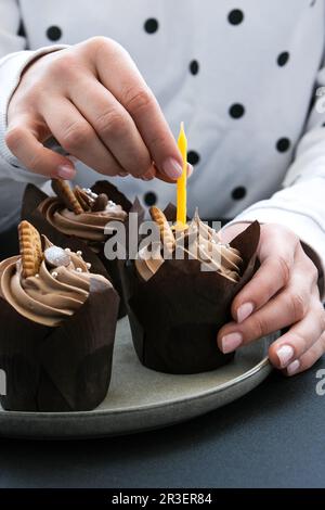 Les mains des femmes font de délicieux petits gâteaux au chocolat avec de la crème sur fond sombre. Trois muffins au chocolat. Gâteau d'anniversaire préparation Banque D'Images