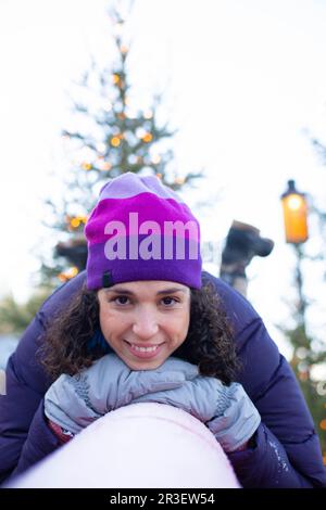 jeune femme brune vêtue d'hiver avec son visage appuyé sur une rampe enneigée rouge avec des arbres en arrière-plan Banque D'Images
