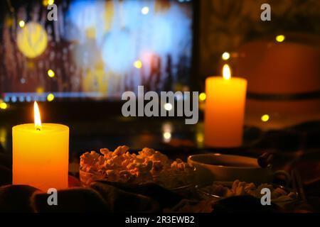 Film sur ordinateur portable la nuit dans la chambre éclairée par des bougies.Pop-corn.Atmosphère d'automne à la maison Banque D'Images