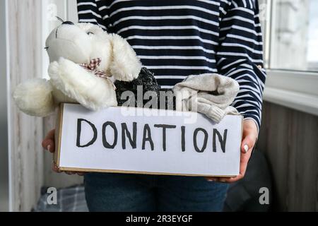 Une femme volontaire tient une boîte de dons avec des jouets et des vêtements usagés à l'intérieur. Bonne charité. Femme méconnaissable boîte de rangement wi Banque D'Images