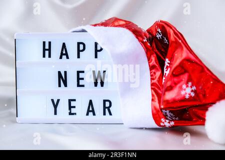 Visionneuse avec texte BONNE ANNÉE avec chapeau de père noël sur fond en tissu de soie. Concept de vacances d'hiver. Banque D'Images