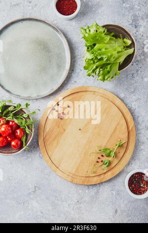 Planche à découper ronde en bois, légumes verts et assaisonnements sur fond clair Banque D'Images