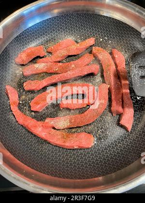 Des lanières de steak fraîchement coupées dans une poêle sont cuites lentement Banque D'Images
