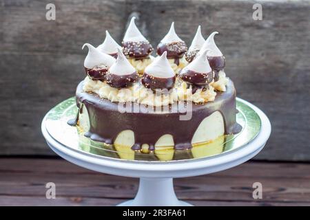 Cheesecake d'anniversaire décoré avec une sauce au chocolat noir fondu, des meringues et des tourbillons de crème au beurre sur le cakestan blanc. Arrière-plan rustique Banque D'Images