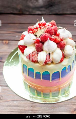 Gâteau rose, violet et bleu avec chocolat blanc fondu, fraises fraîches enrobées de chocolat, framboises, cassis et meringues Banque D'Images