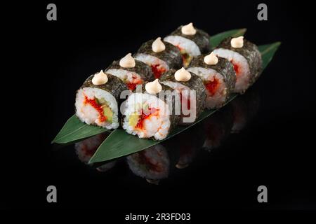 Délicieux sushi traditionnel frais sur fond noir avec reflet. Petit pain à sushis avec riz, nori, fromage à la crème, tobi Banque D'Images