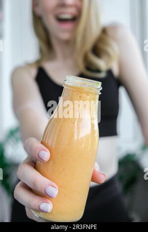 Jeune femme blonde millénelle boit du smoothie végétalien Detox. Femme faisant des exercices de yoga à la maison. Manger propre, perte de poids, Banque D'Images