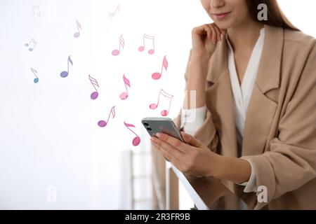 Femme écoutant de la musique sur un téléphone mobile à l'intérieur, gros plan. Illustrations de notes de musique provenant du gadget Banque D'Images