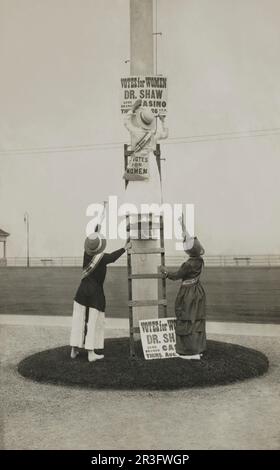 Trois femmes installant un panneau publicitaire d'un événement de suffrage. Banque D'Images