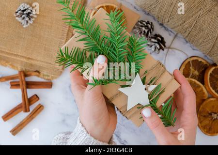 Femme faisant boîte avec les cadeaux du nouvel an, enveloppé dans du papier artisanal et décoré avec branche de sapin. Concept de vacances et de cadeaux. Handma Banque D'Images