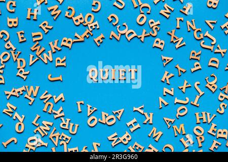 Mot QUIET fait de lettres en bois sur fond bleu clair. Concept de citations de mots de motivation. Banque D'Images
