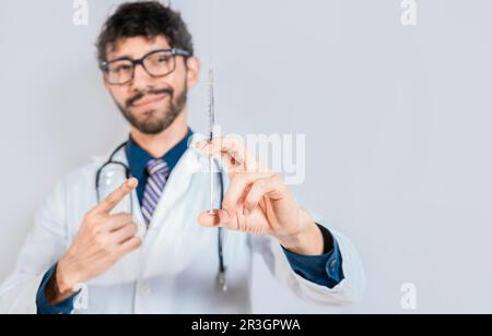 Beau médecin tenant et pointant une seringue isolée. Médecin souriant montrant une seringue sur fond isolé. Concept de médecin et de vaccin Banque D'Images