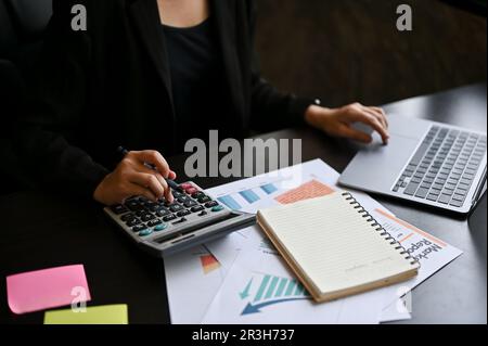 Une femme d'affaires calcule les ventes à l'aide d'une calculatrice et d'un ordinateur portable à son bureau. image rognée Banque D'Images