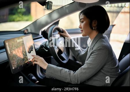 Chiang Mai, Thaïlande - 23 mai 2023: Une femme d'affaires asiatique réussie et attrayante utilisant un système de navigation GPS, en sélectionnant une destination sur un dashboa Banque D'Images