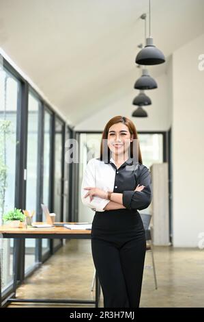 Portrait d'une femme d'affaires asiatique millénaire attrayante et confiante, souriante et debout avec les bras croisés dans son bureau moderne. Banque D'Images