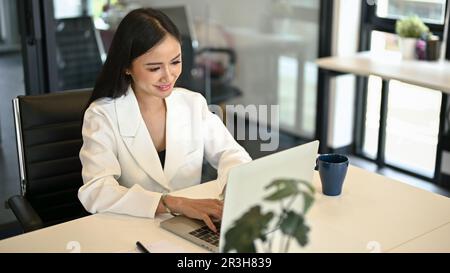 Femme d'affaires asiatique prospère et confiante travaillant dans son entreprise travaille sur un ordinateur portable dans son bureau. Banque D'Images