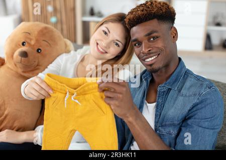 jeune couple de course mixte tenant des vêtements de bébé Banque D'Images
