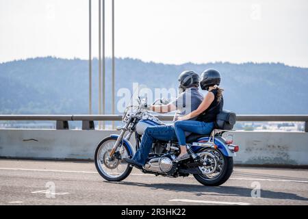 Un homme et une femme heureux portant un casque en grande forme physique font des courses le long de la route sur une moto classique sur un pont haut en profitant de la bonne wea Banque D'Images