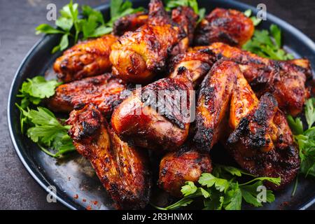 Des ailes de poulet et des pilons de poulet au barbecue traditionnel avec du piment et de la coriandre chauds servis en gros plan sur une assiette rustique Banque D'Images