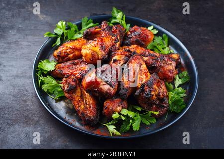 Des ailes de poulet et des pilons de poulet au barbecue traditionnel avec du piment et de la coriandre chauds servis en gros plan sur une assiette rustique Banque D'Images