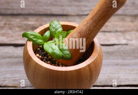 Mortier avec grains de poivre et basilic sur table en bois, gros plan Banque D'Images