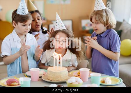 Portrait de la petite fille mignonne soufflant des bougies sur le gâteau pendant la fête d'anniversaire avec des amis. Banque D'Images