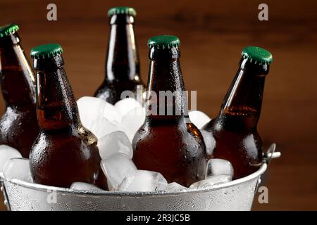 Seau en métal avec bouteilles de bière et glaçons sur fond de bois, gros plan Banque D'Images
