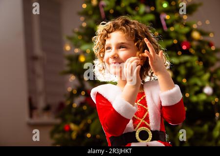 Adorable fille en robe de Noël près de l'arbre de noël classique décoré Banque D'Images