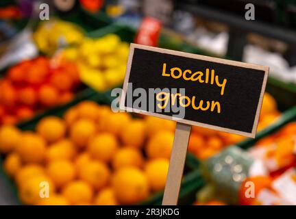 Affiche d'étiquette d'information en bois avec texte CULTIVÉ LOCALEMENT contre le message relatif aux étagères défocacées du magasin. Soutenir les agriculteurs locaux récolte Banque D'Images