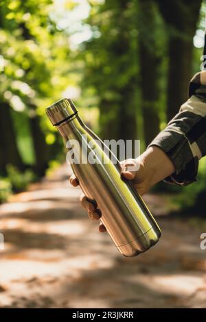 Gros plan d'une bouteille d'eau pour la main d'une femme méconnue. Bouteille d'eau thermique en acier réutilisable dans le parc. Style de vie durable. Banque D'Images