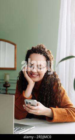 Jeune heureuse souriante jolie femme tenant un smartphone utilisant la technologie moderne de téléphone portable, regardant le mobile, la vérification des applications de téléphone cellulaire, regardant social moi Banque D'Images