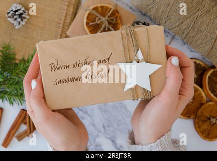 Voeux chaleureux et bonhomme de neige kisses inspiration plaisanterie citation phrase femme faisant Box avec les cadeaux du nouvel an, enveloppé dans papier d'artisanat et Banque D'Images