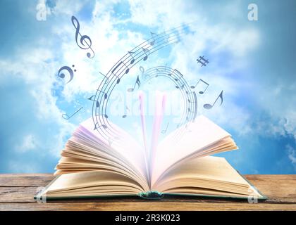 Musique provenant du livre. Symboles musicaux volant au-dessus du dôme sur une table en bois contre le ciel Banque D'Images