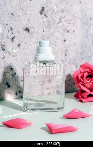 Bouteille de parfum en verre et fleur rose corail avec pétales sur fond de pierre naturelle au soleil, gros plan Banque D'Images