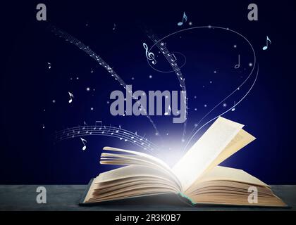 Musique provenant du livre. Symboles musicaux survolant le dôme sur une table en bois sur fond bleu foncé Banque D'Images