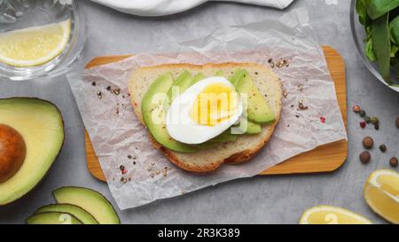 Délicieux sandwich avec œuf dur, morceaux d'avocat et feuilles de basilic sur table grise, plat Banque D'Images