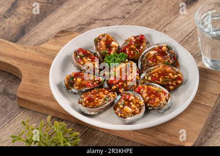 Délicieux ormeaux cuits à la vapeur avec sauce tomate épicée, sauce cinq saveurs taïwanaises sur fond de table en bois. Banque D'Images