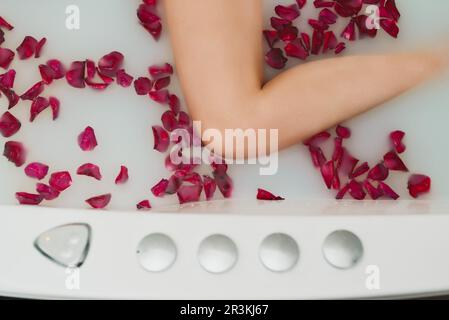 La femme est dans un bain avec du lait et des pétales de rose. Banque D'Images
