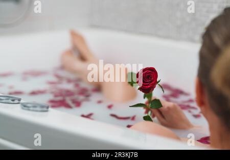 Une femme se détend dans un bain avec du lait et des pétales de rose. Banque D'Images